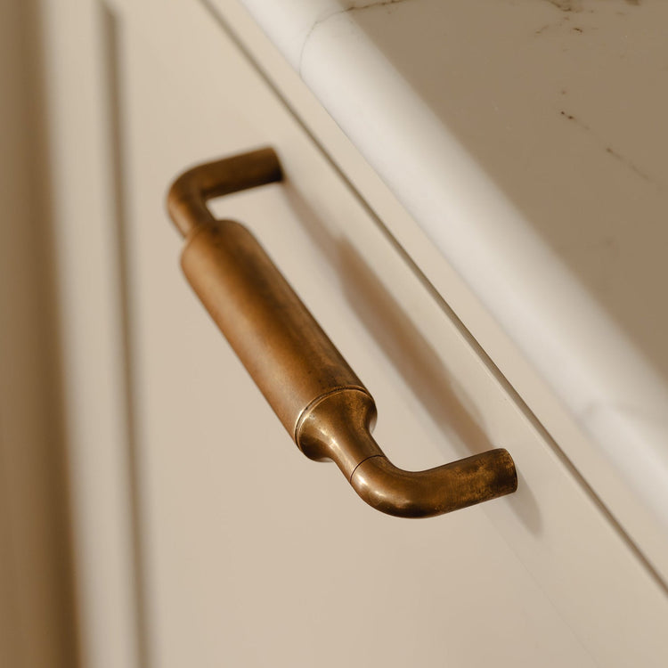 Close-up of a kitchen cabinet with a marble countertop and brass handle.